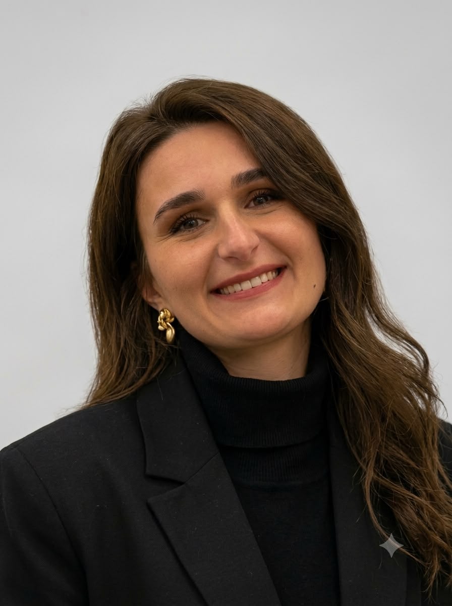 A professional studio portrait of Albina Musliu, a young and dynamic educator. She is wearing a modern professional blouse, looking directly at the camera with a focused and intelligent gaze. The background is a clean off-white wall with subtle architectural shadows, maintaining a minimalist and corporate aesthetic.
